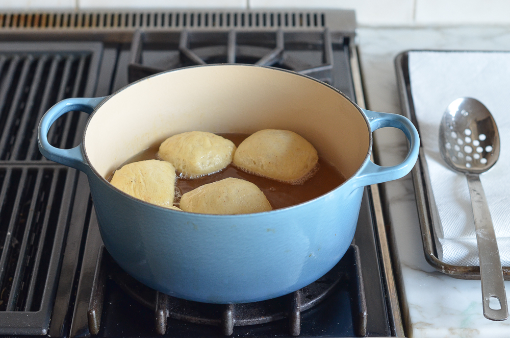 Pieces of dough frying in oil in a Dutch oven.