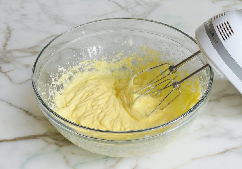 Electric mixer in a bowl of yellow creamed mixture.