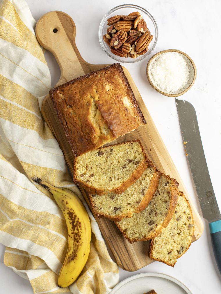 banana bread with coconut and pecans on cutting board with plaid yellow cloth