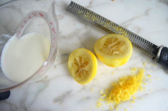 Zested and squeezed lemons next to measuring cup of milk.
