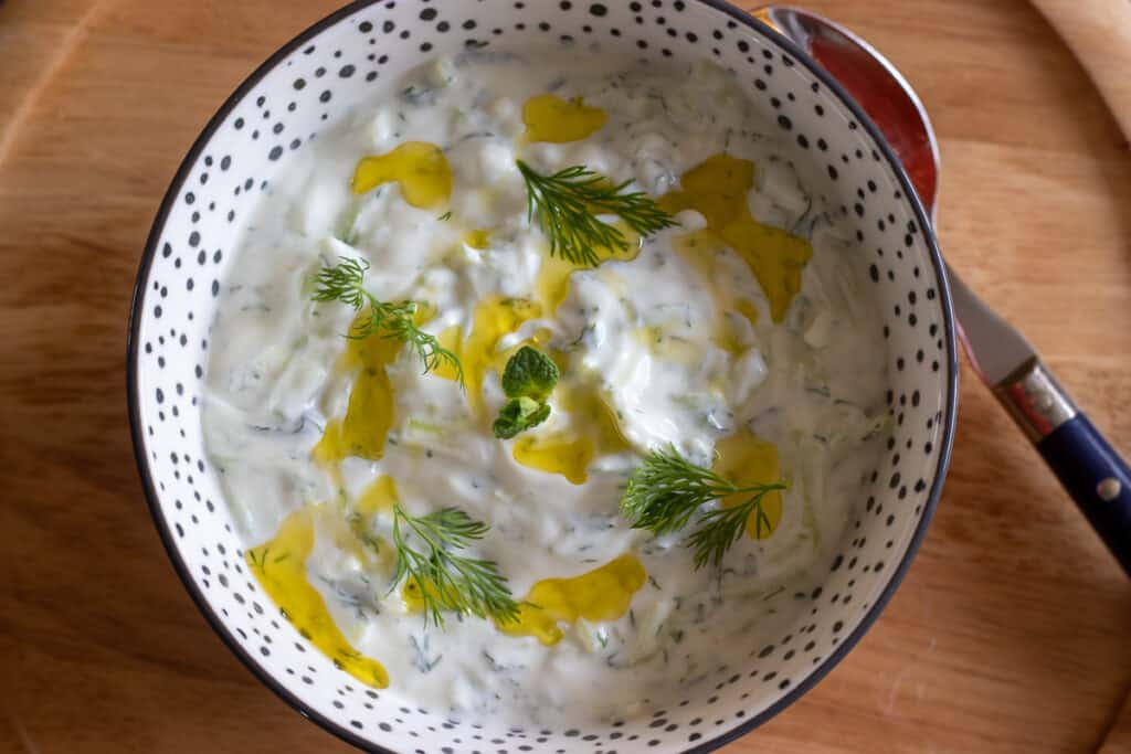 Cacik is served in a bowl with a drizzle of olive oil and fresh herbs