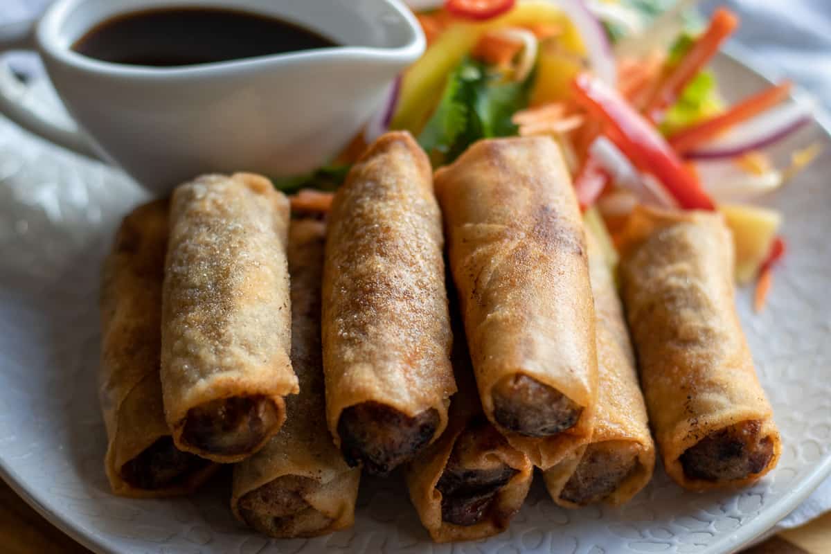 duck rolls are served on a plate with salad and hoisin sauce