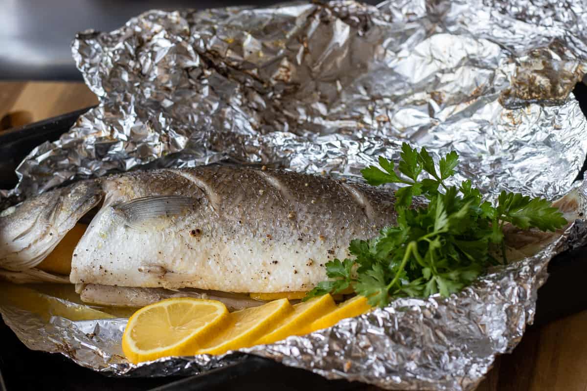 whole baked sea bass in foil served with lemon slices
