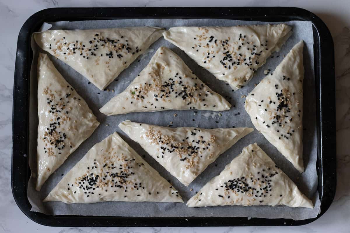borek pieces are brushed with the sauce and sprinkled on sesame seeds