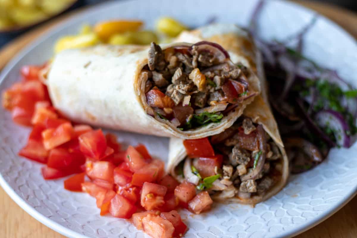 tantuni wrap cut in half and served on a plate with side of chopped tomatoes and onion salad