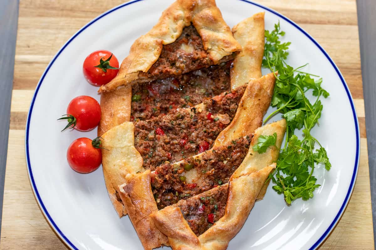 Turkish Kiymali Pide is served on a plate with tomatoes and parsley