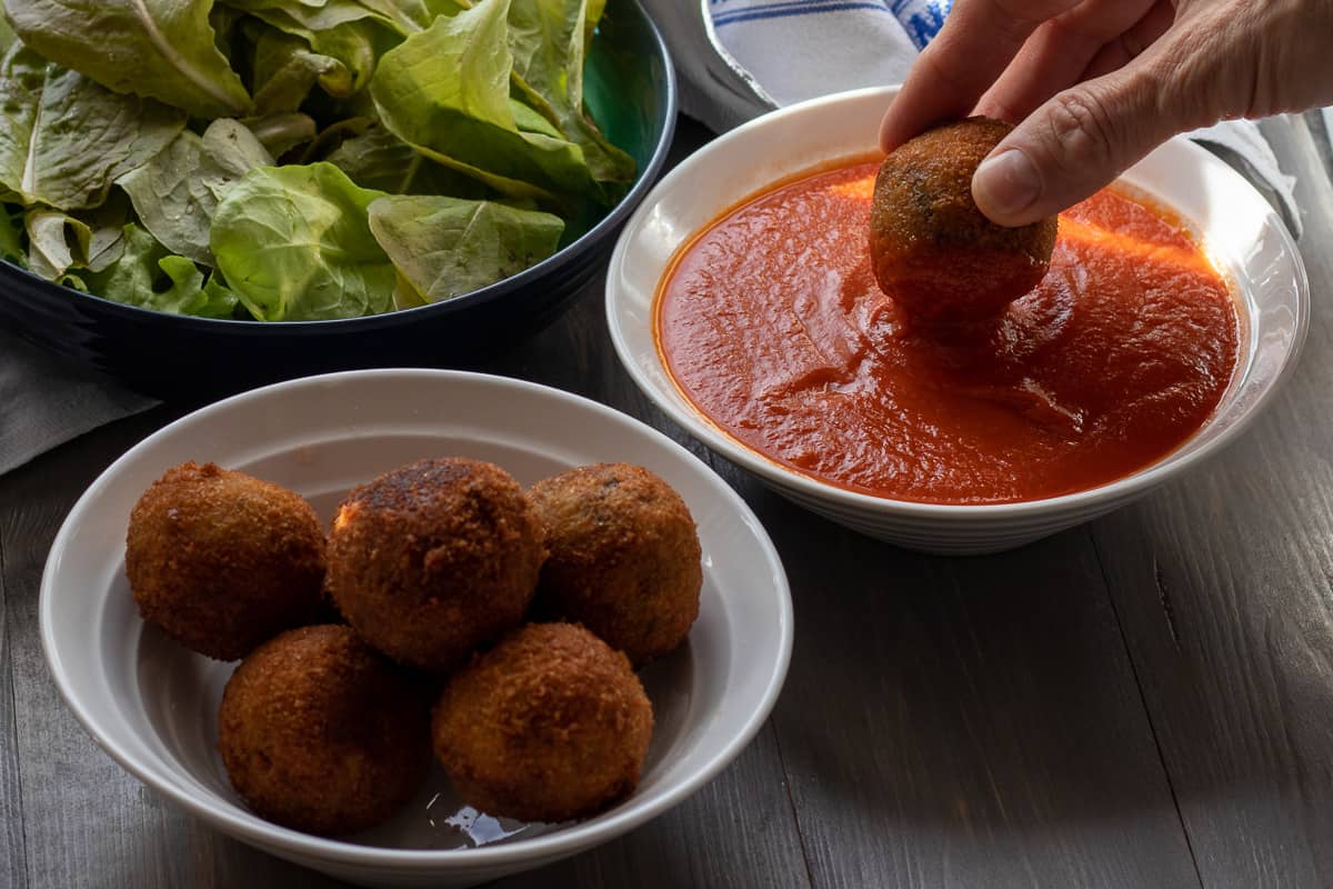 arancini is dipped into tomato sauce