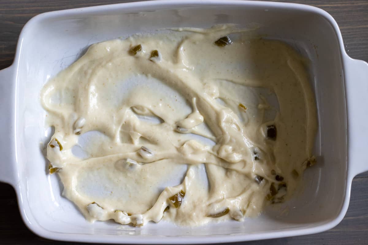 a spoonful of white sauce is spread on a bottom of a baking dish