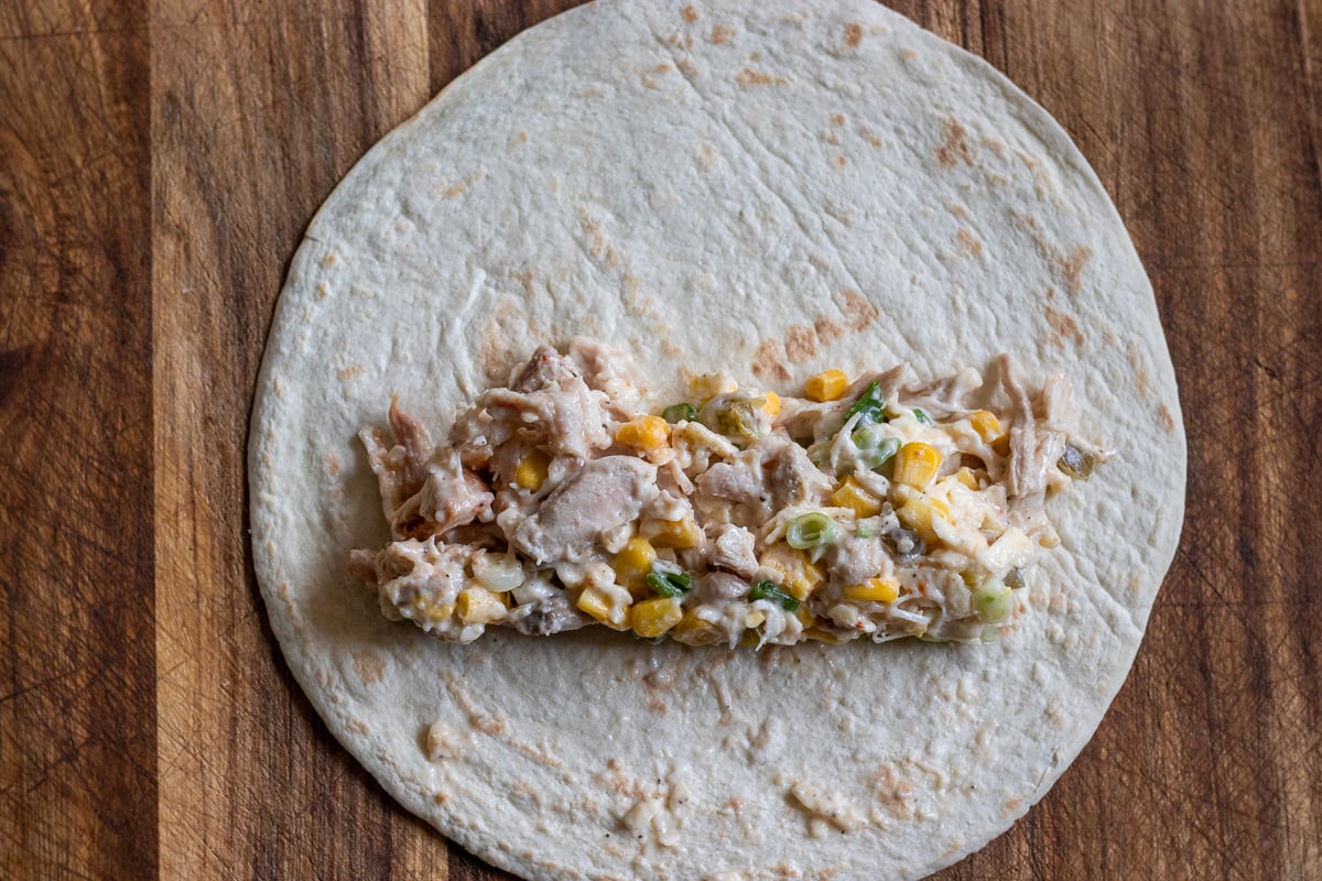 a spoonful of chicken filling is spread on a flour tortilla
