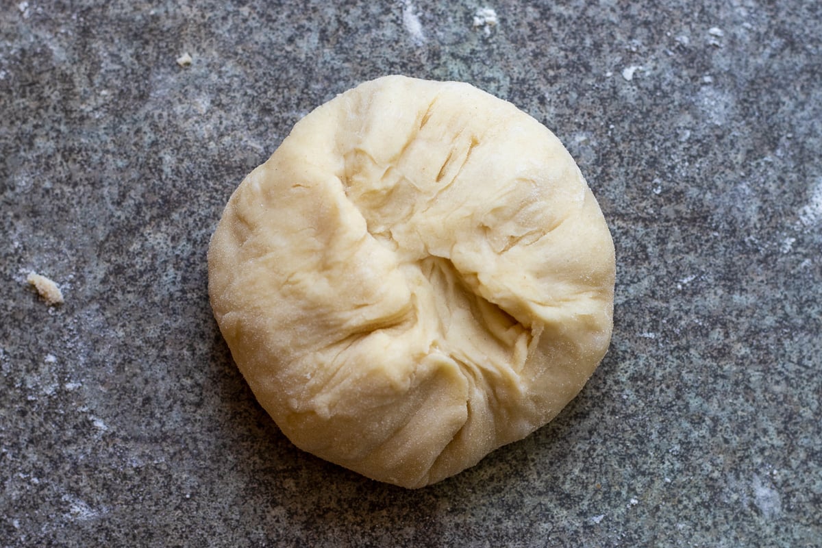 shaping a piece of dough into a ball by pinching the edges into the middle