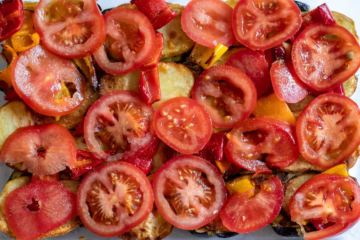 Sliced tomatoes and peppers are arranged on top of the potatoes