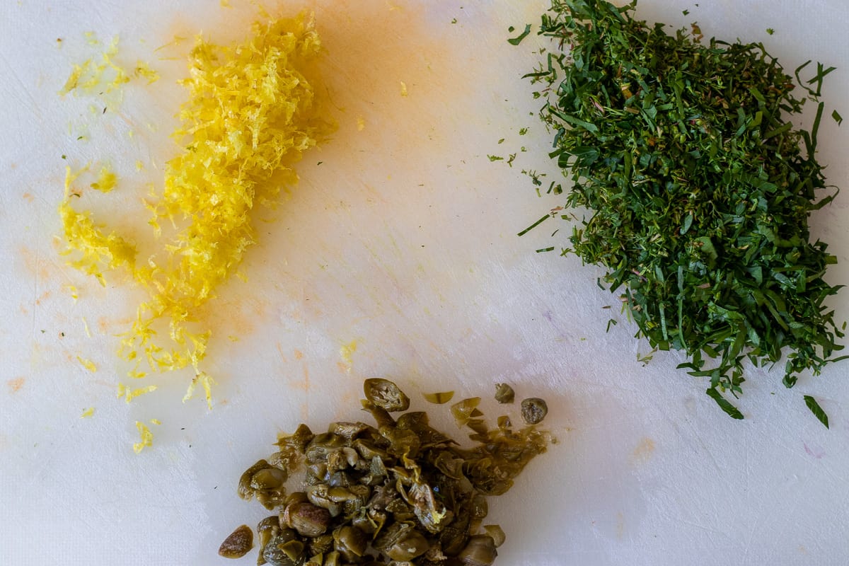 lemon zest, chopped herbs and capers on a cutting board
