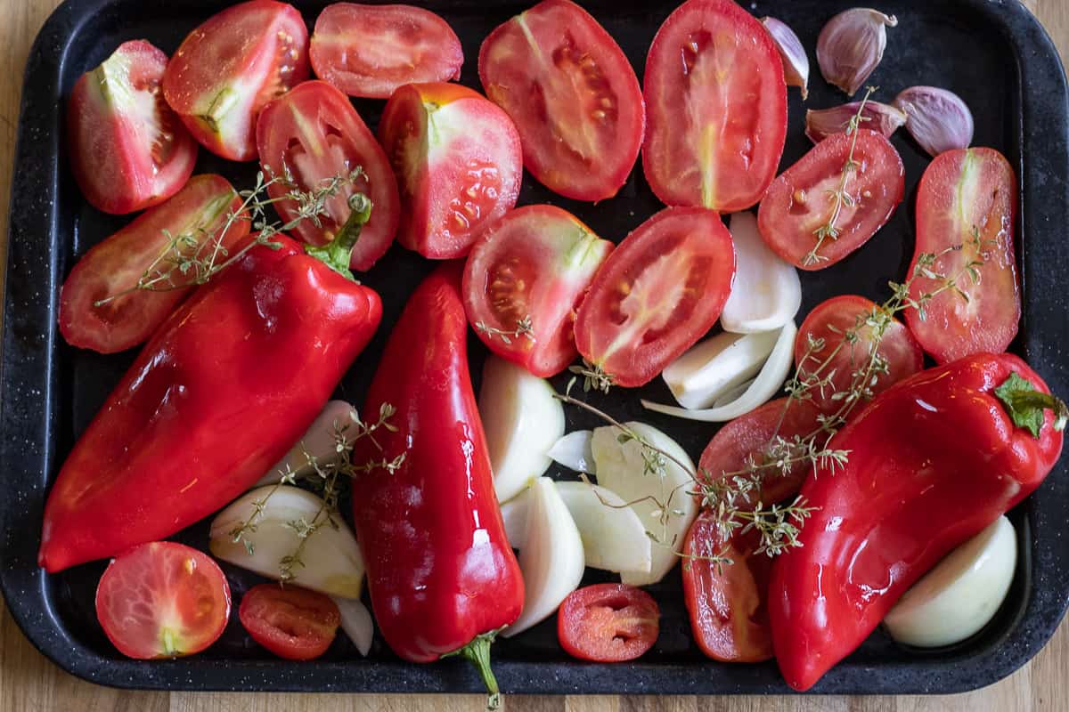 red peppers, tomatoes, onions and garlic are on a baking tray