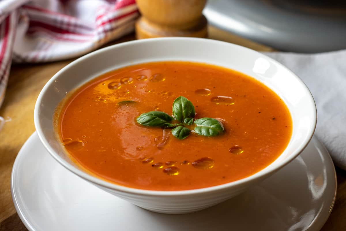 red pepper and tomato soup served in a bowl and garnished with olive oil and basil