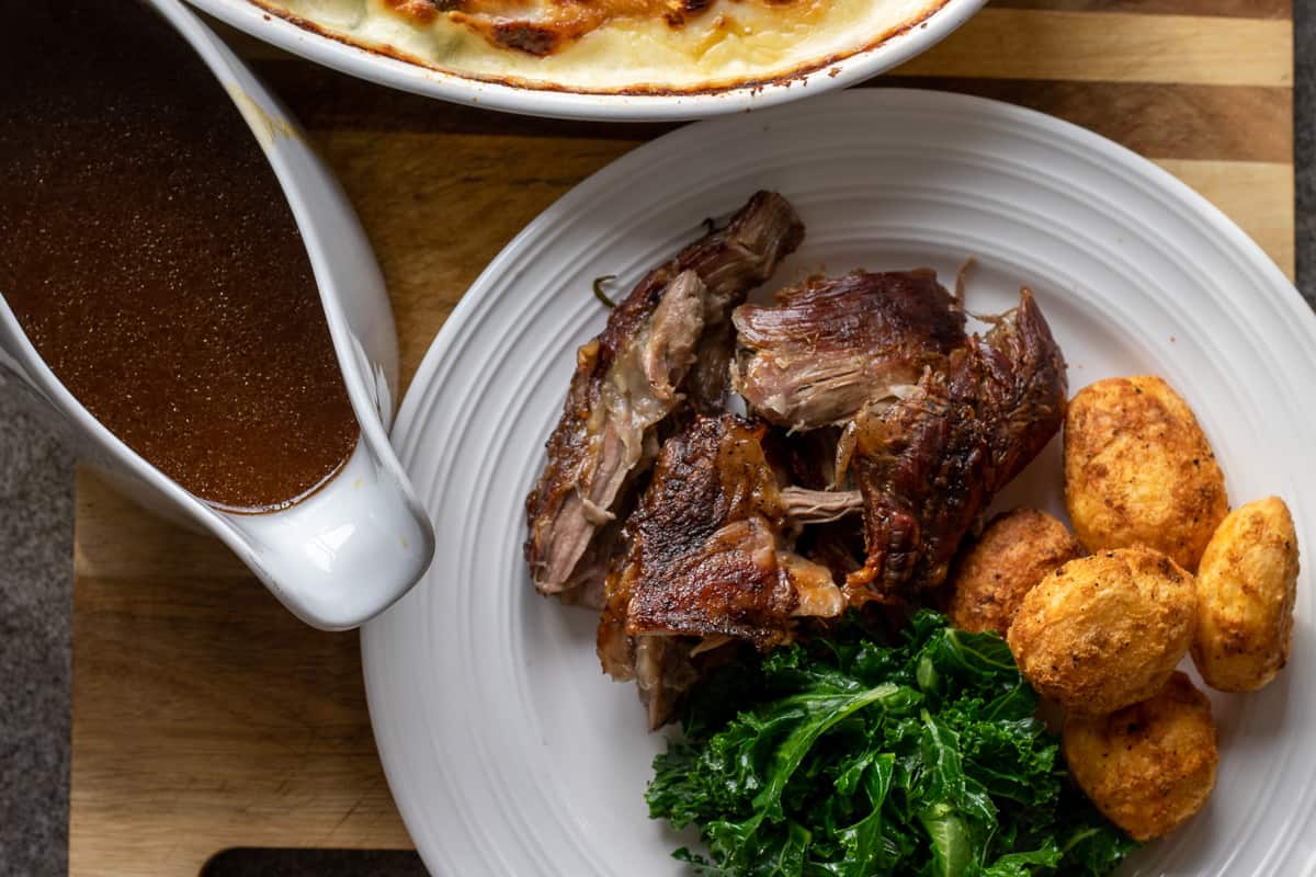 lamb shoulder meat is served with roast potatoes, greens and gravy