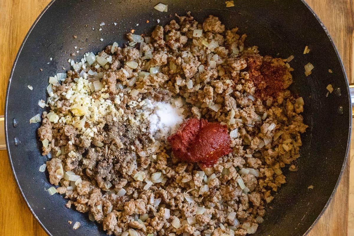 Seasoning and tomato paste are added to sautéed onions and minced lamb