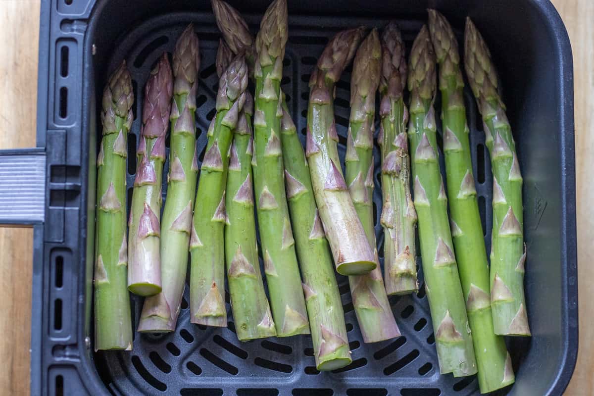 asparagus are placed in an air fryer basket in a single layer