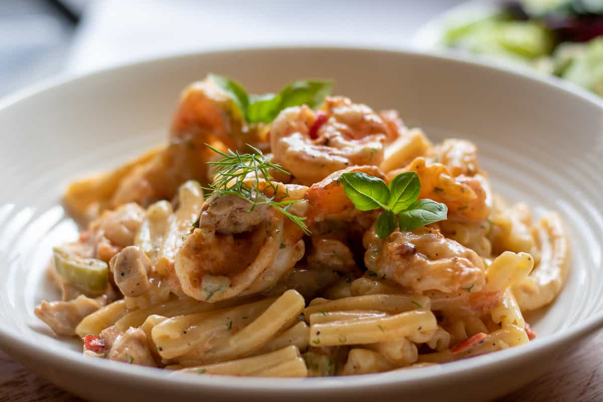 Cajun Chicken and shrimp pasta served in a bowl with dill and basil leaves.
