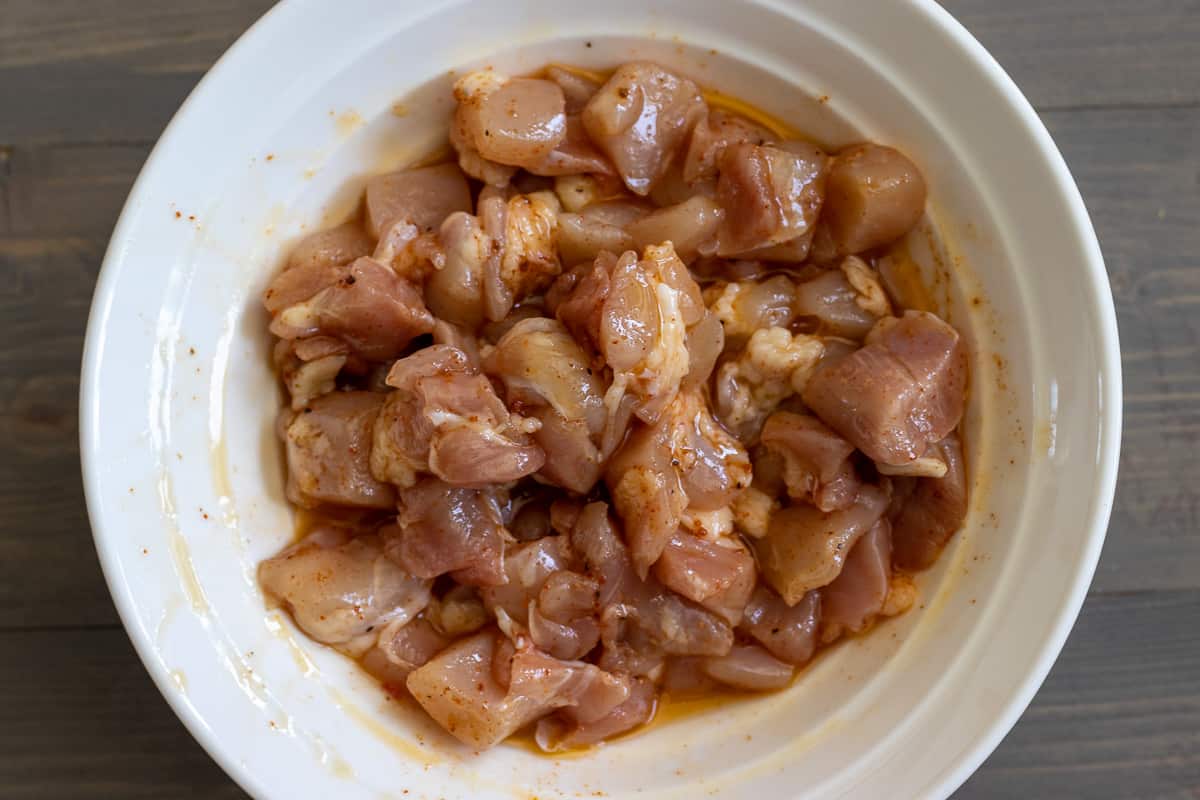 Marinated chicken pieces with olive oil and cajun spices in a bowl.