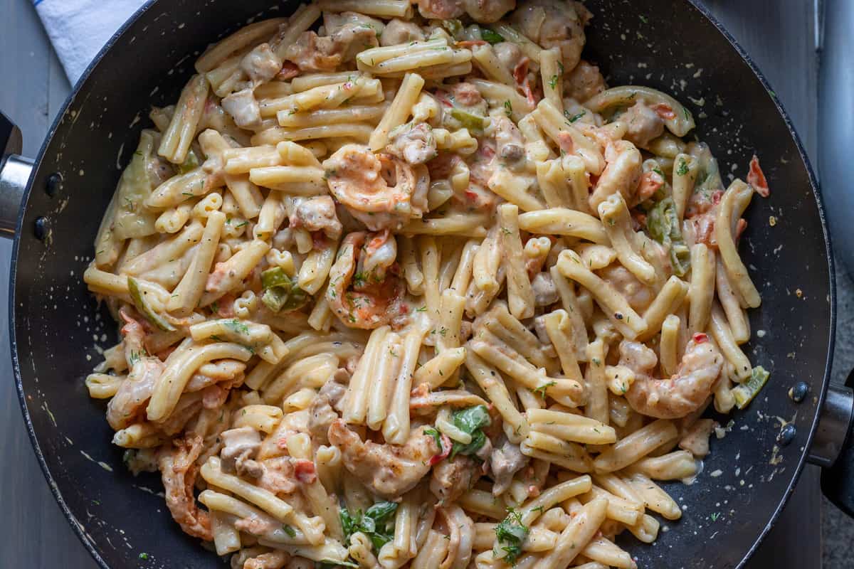cooked pasta is mixed with the sauce, cooked prawns and chicken pieces