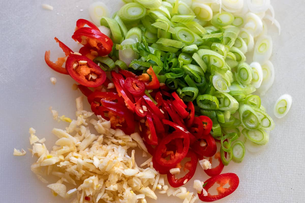 finely chopped spring onions, chillies and garlic on a cutting board