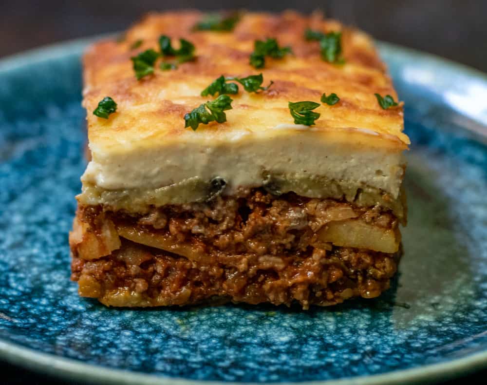 A slice of greek moussaka served on a plate with some chopped parsley