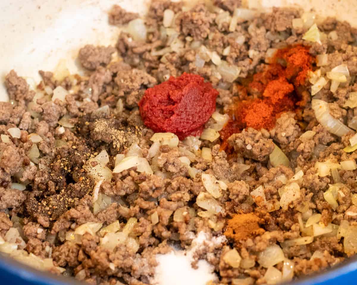 Seasoning and tomato paste goes into meat sauce.