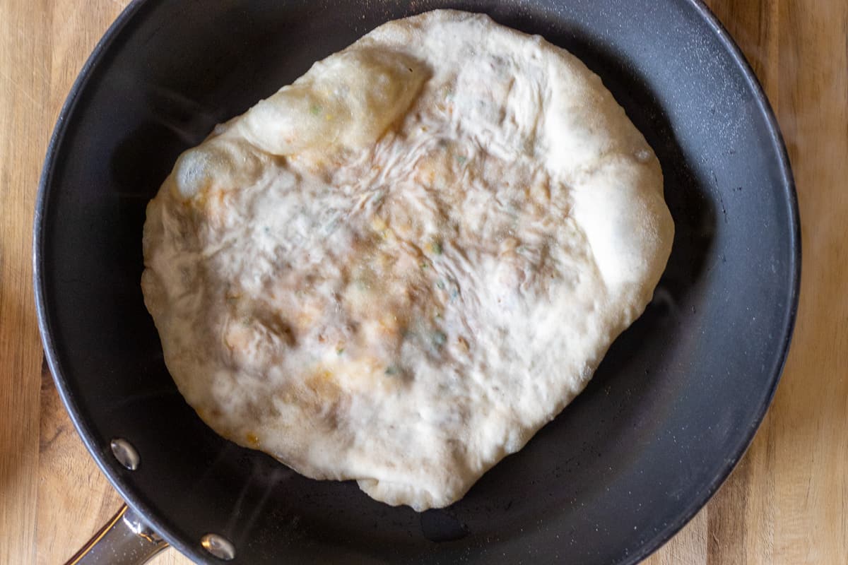 the naan is placed in a hot pan and cooked until golden brown