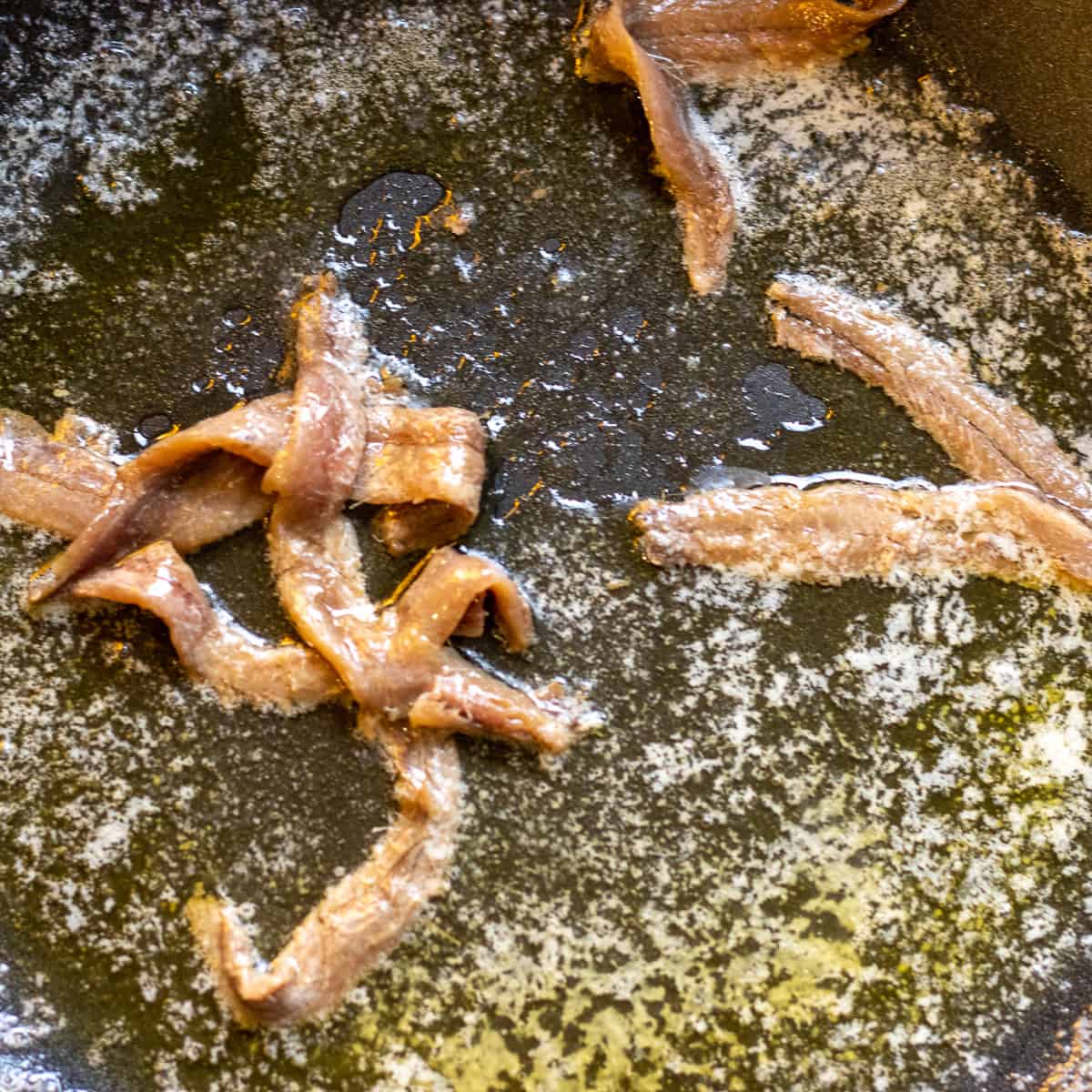anchovies are cooking with butter in a wok