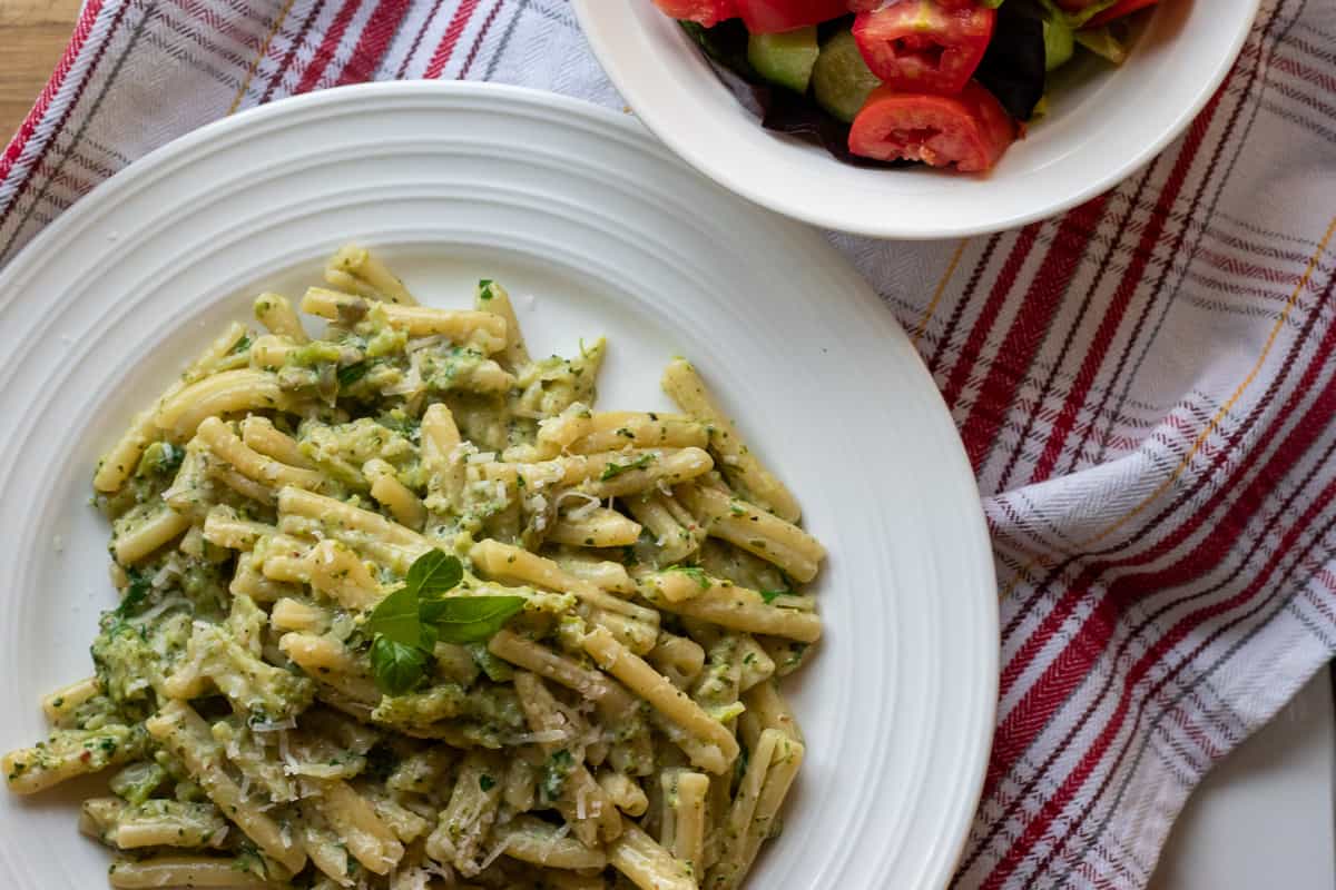 a portion of pasta with green sauce is served with a bow; of salad