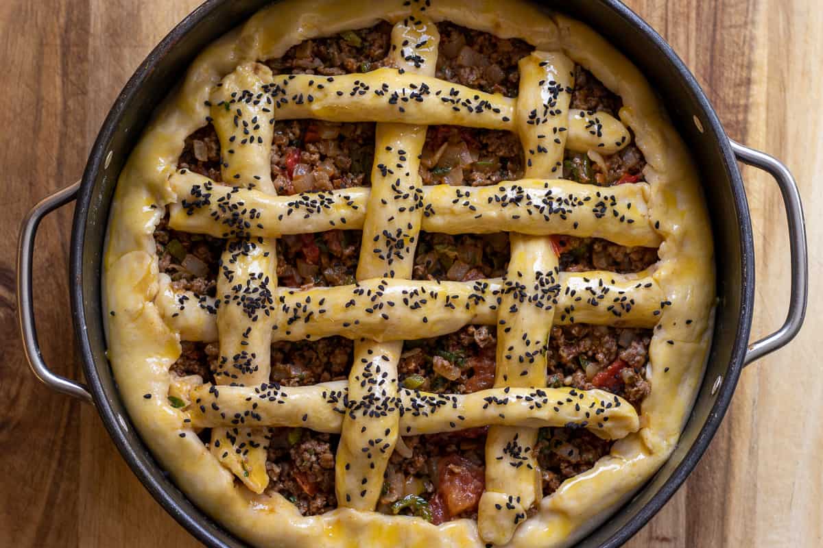 the pie is decorated with pastry strips, egg washed and sprinkled with nigella seeds