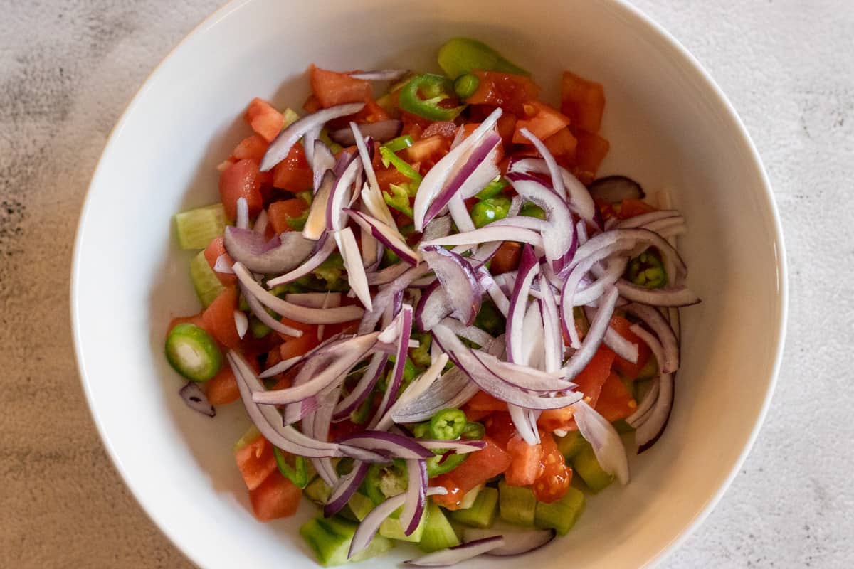 Thinly sliced peppers and onions are added to the bowl