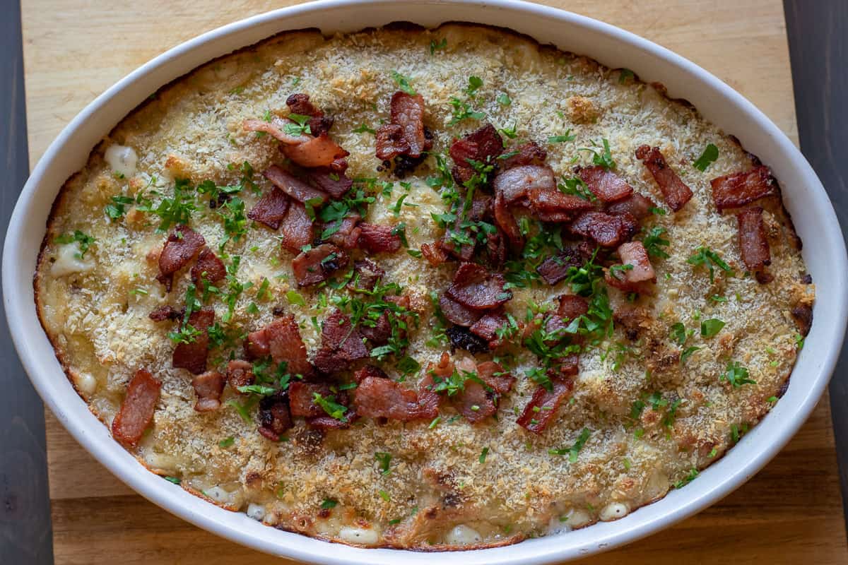 baked Mac and cheese is garnished with crispy bacon pieces and chopped parsley 