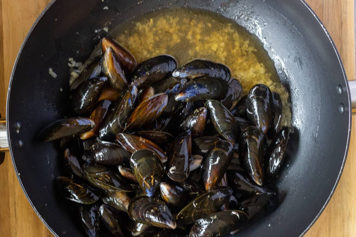 The wine and the mussels are added to the pan