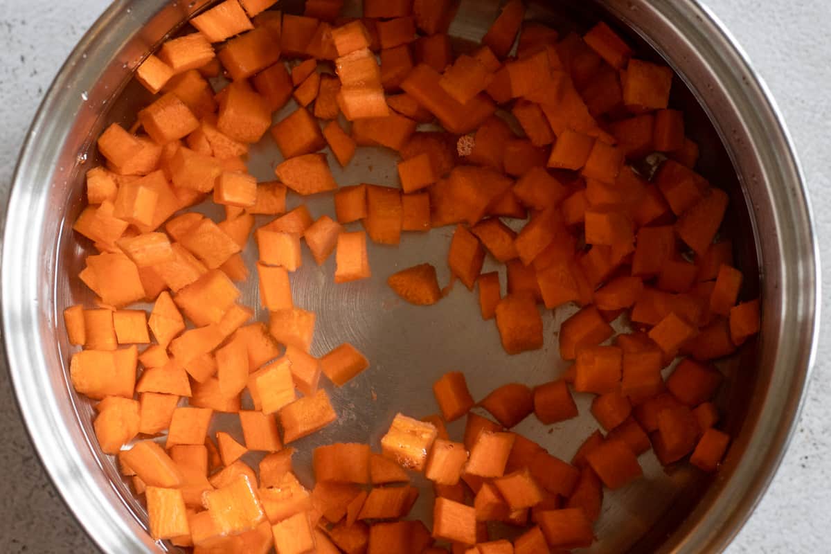 peeled and diced carrots are in a pan filled with cold water