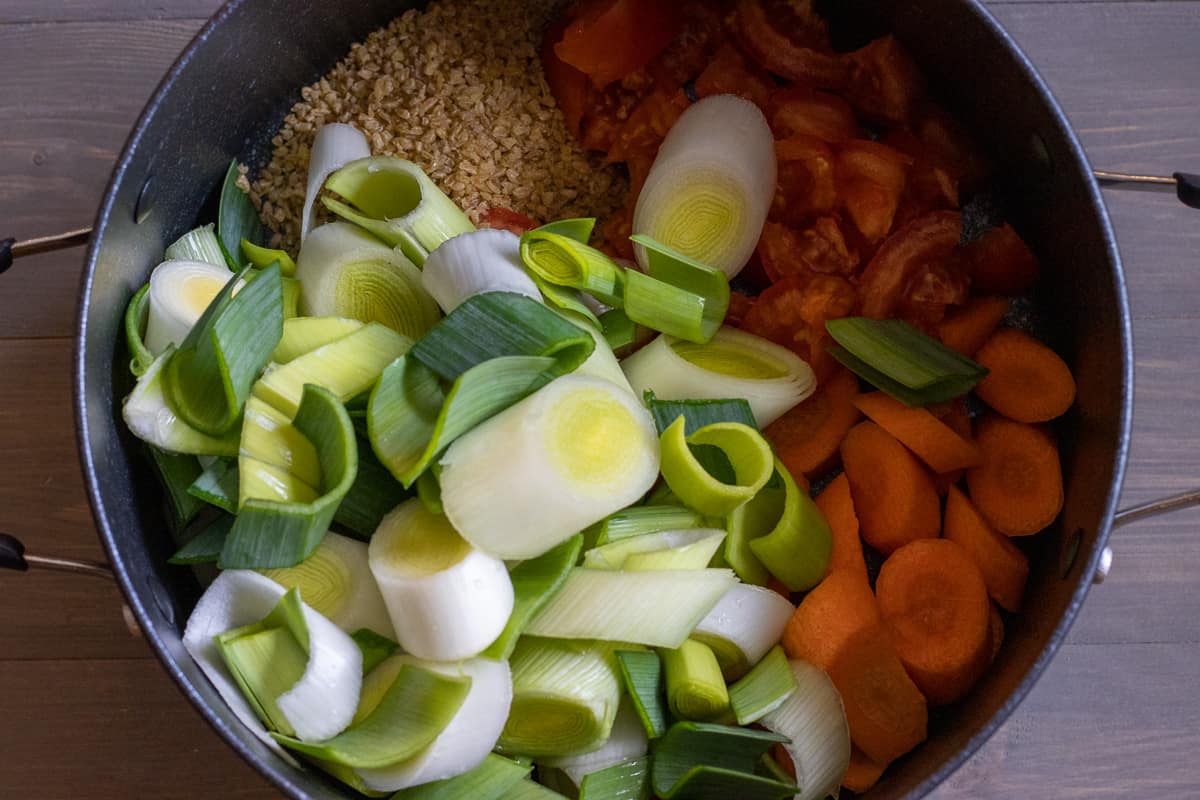 leeks, carrots, bulgur and tomatoes are placed in a pan