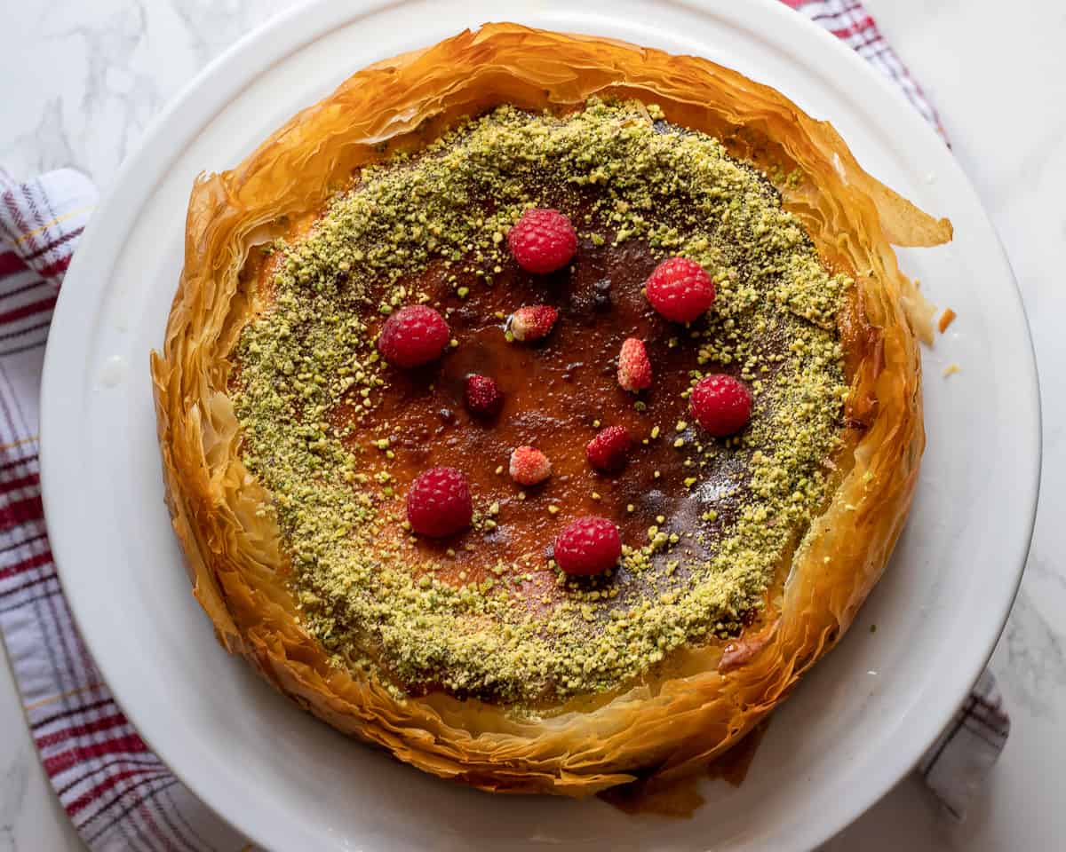 baklava cheesecake is garnished with chopped pistachio and red berries