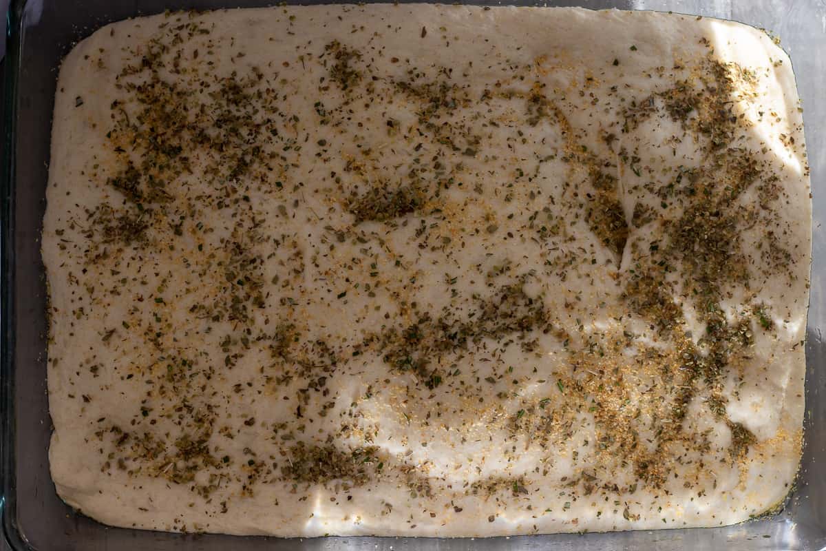 the dough is sprinkled with oregano, garlic powder, and cheese