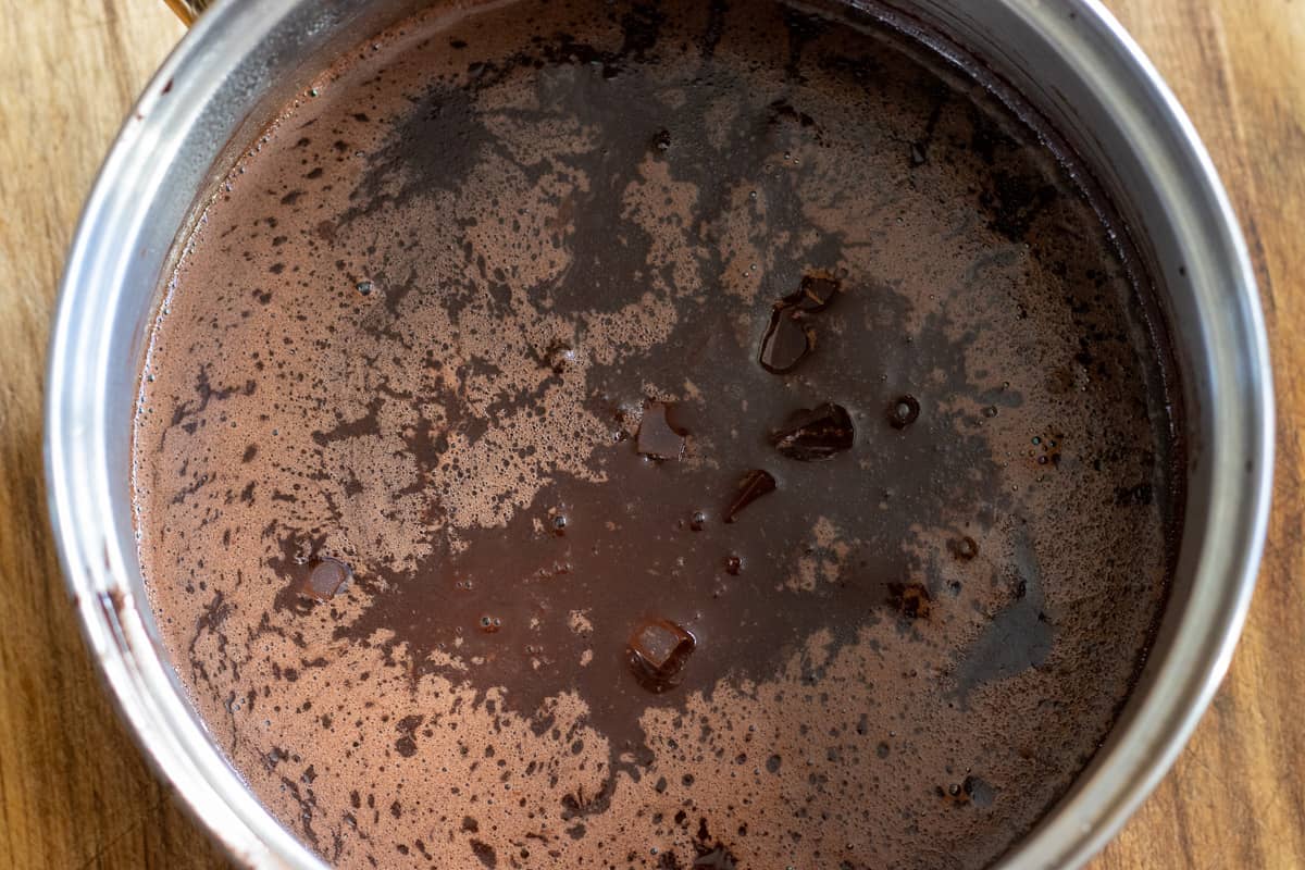 Chocolate pieces are added to hot mixture of milk, sugar, butter and cacao powder