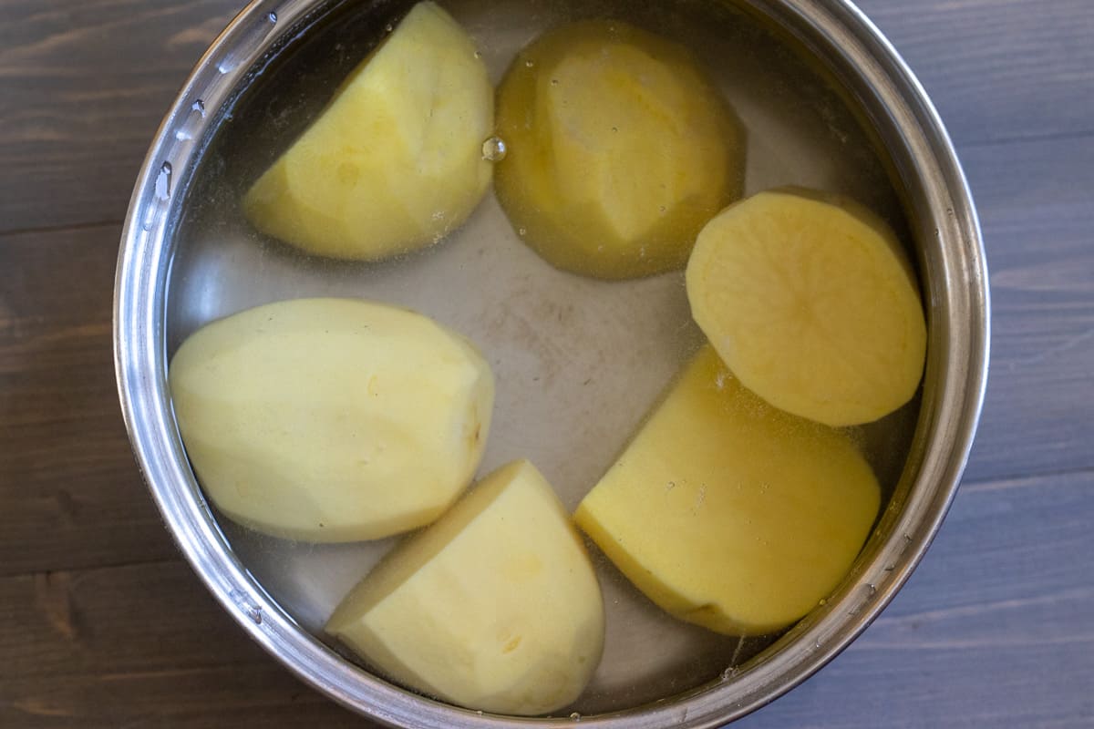 potatoes are peeled, cut in halves, and placed in a pot filled with cold water