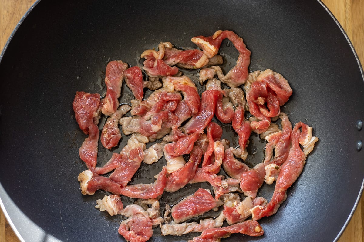 stir frying the marinated beef strips in a wok