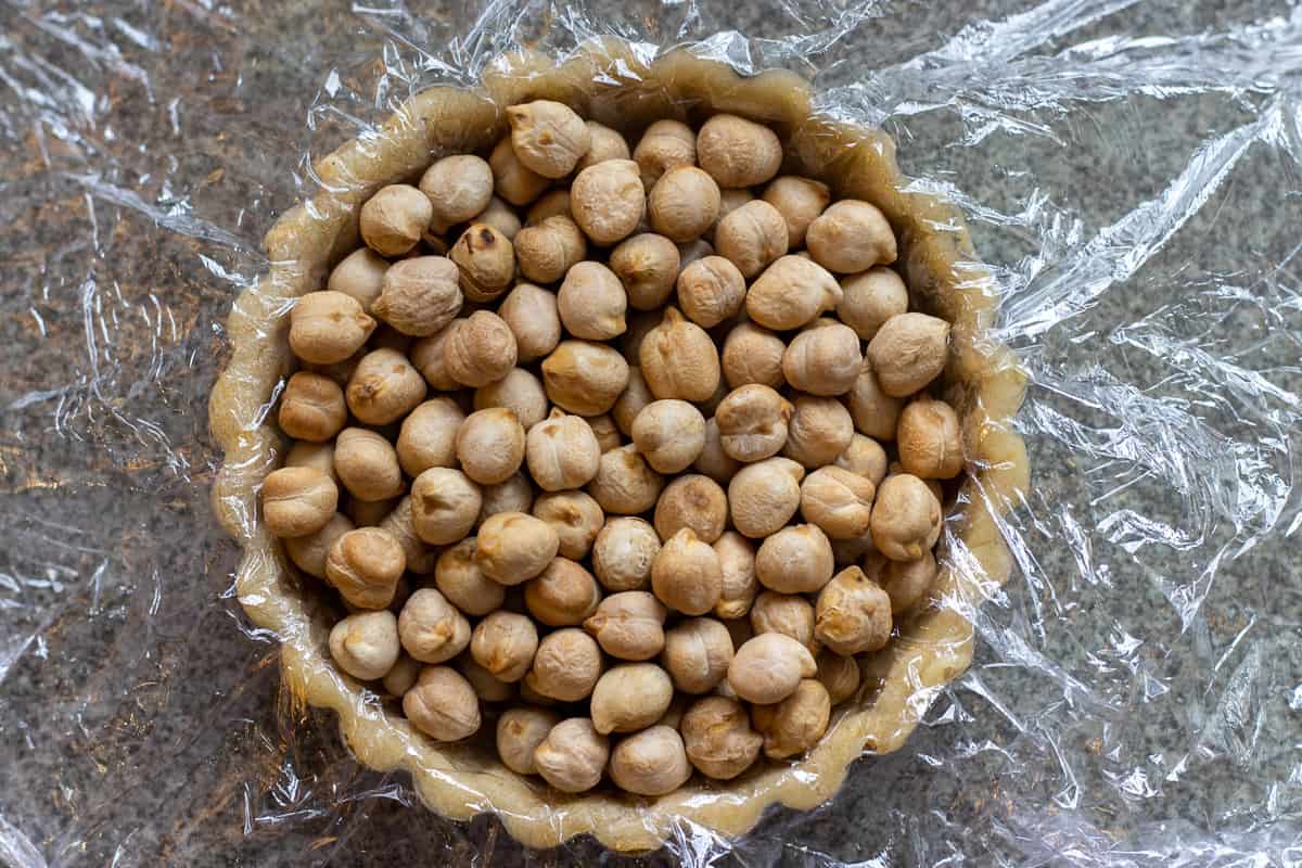 the tartlet dough is covered with cling film and filled with chickpeas