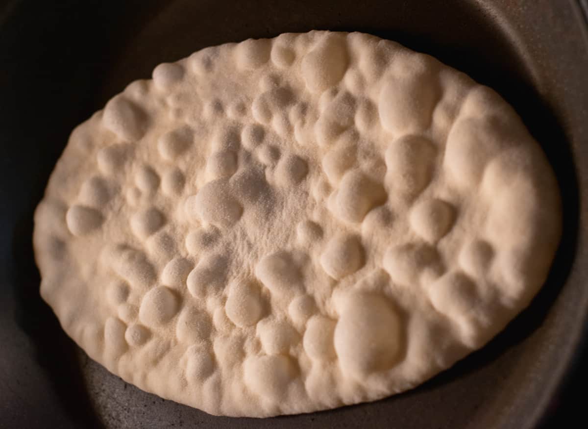 naan dough circle is cooking on a hot pan