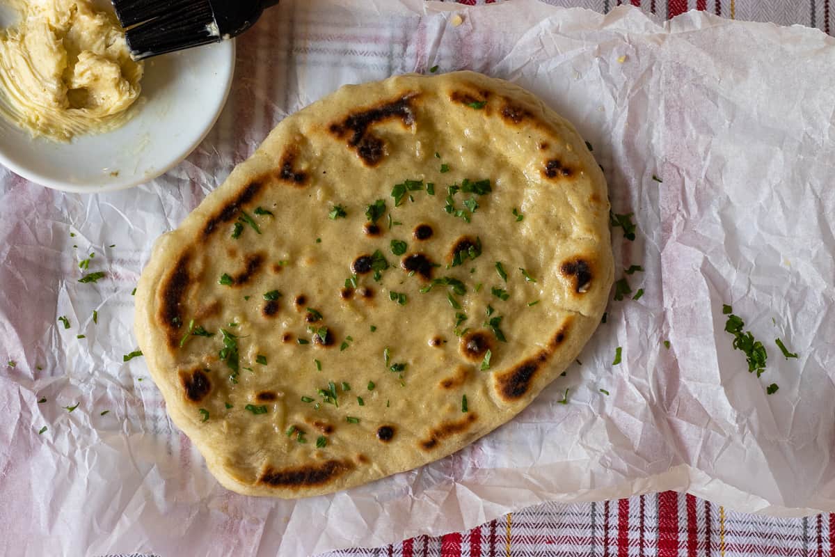 Naan is cooked until golden brown and brushed with garlic butter
