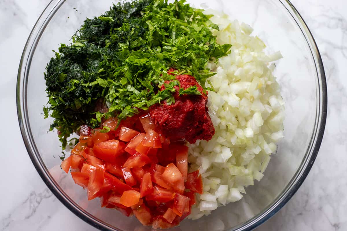 tomatoes, herbs, onions, meat, and rice are placed in a bowl