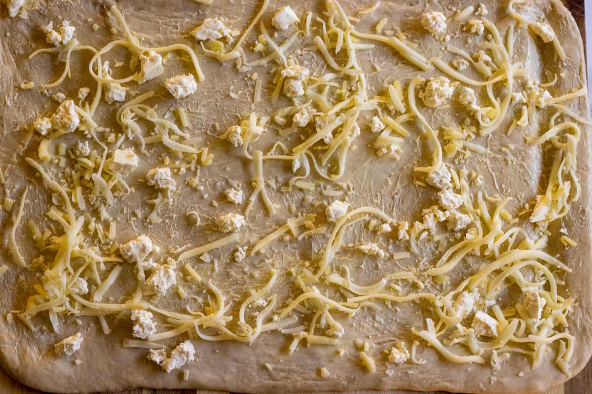 soft butter is spread and cheese is sprinkled on pitka dough