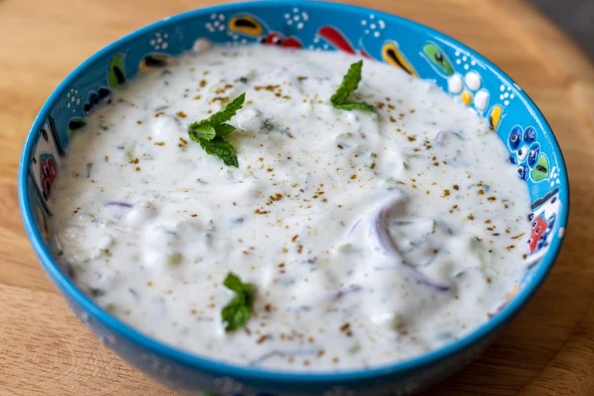 onions and cucumber raita served in a bowl with mint tips