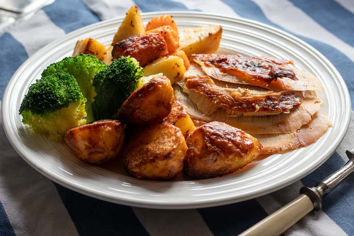 a plate with a few slices of roast turkey meat, broccoli, and roast potatoes
