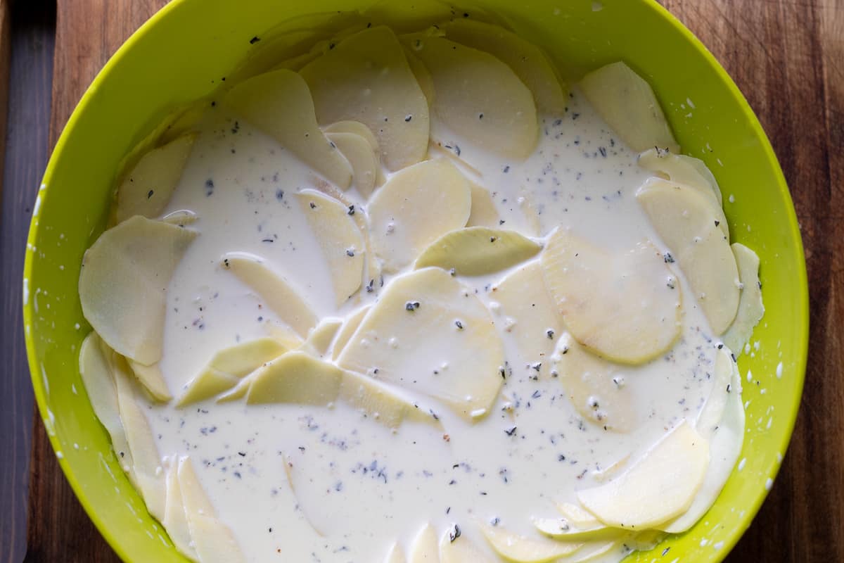 sliced potatoes are mixed with cream mixture in a large bowl