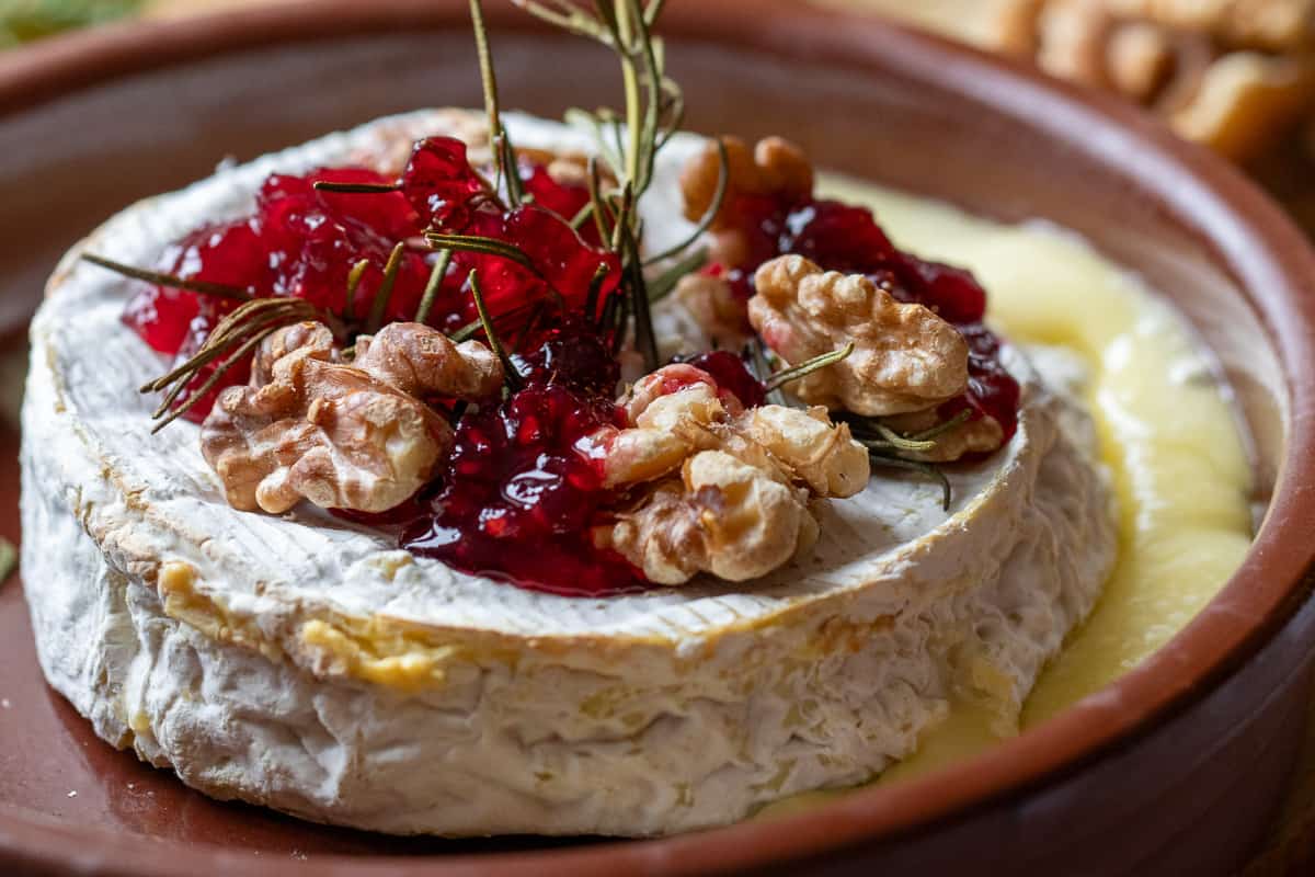 baked brie is topped with walnuts, rosemary, and jam 